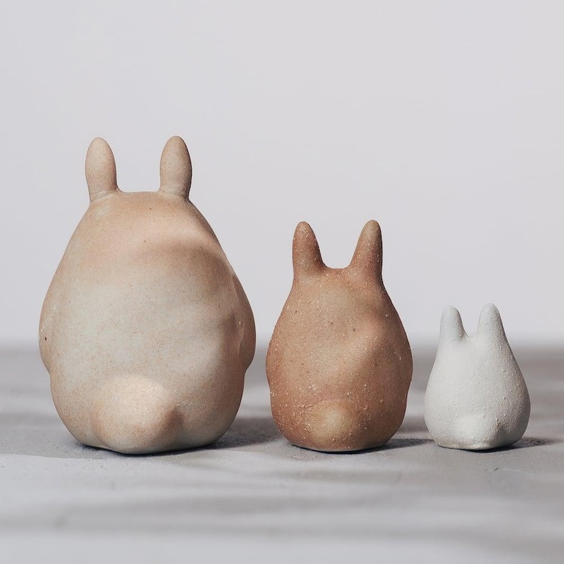 May include: Three ceramic bunny figurines in varying sizes and colors. The largest is a light beige, the middle one is a warm brown, and the smallest is white. Each has upright ears and a rounded body, perfect for home decor.