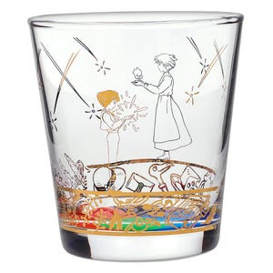 May include: Clear glass tumbler featuring a gold and black illustration of two figures and a small flame. The bottom of the glass has a gold band with colorful accents. The design is reminiscent of an animated film.