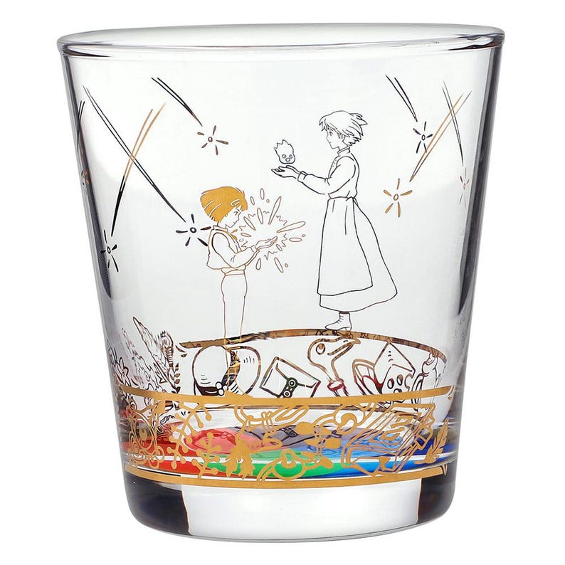 May include: Clear glass tumbler featuring a gold and black illustration of two figures and a small flame. The bottom of the glass has a gold band with colorful accents. The design is reminiscent of an animated film.