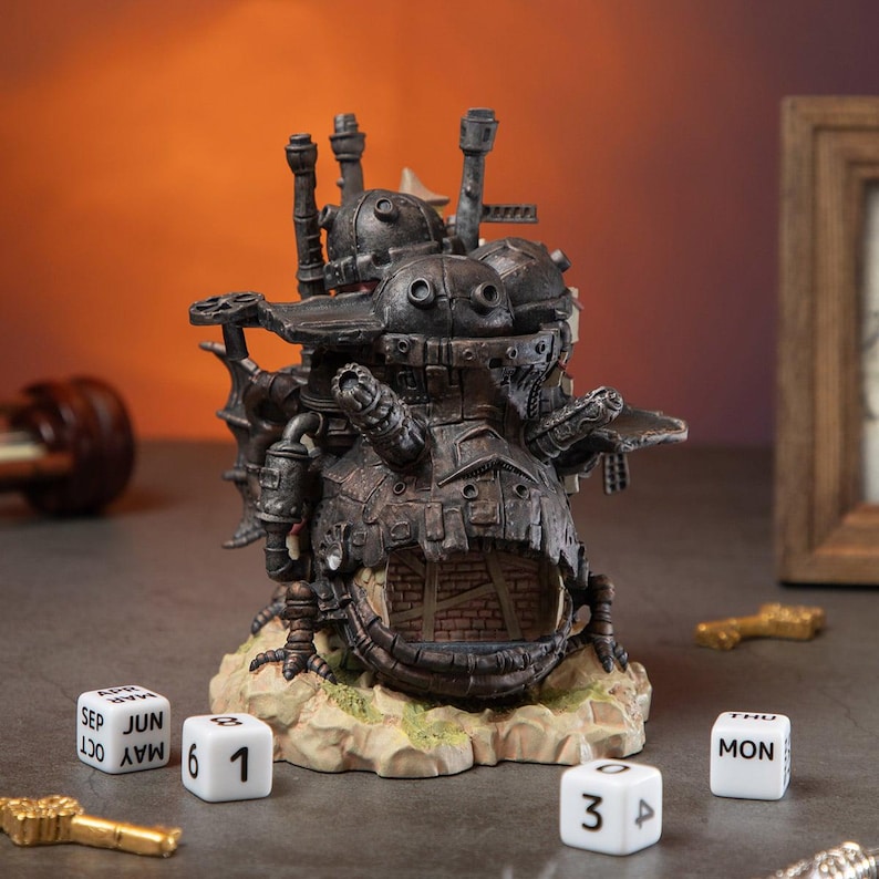 May include: A detailed, dark gray miniature of a fantastical, steampunk-style building with chimneys and mechanical details. The base is a light tan with green accents. White dice with numbers and months are scattered around the base.