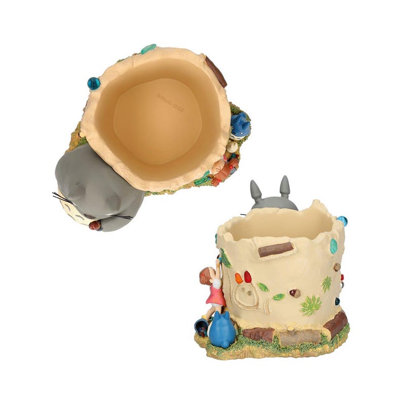 Puede incluir: Un portal&aacute;pices caprichoso con un dise&ntilde;o de tronco de &aacute;rbol con una figura gris de Totoro y una ni&ntilde;a trepando por el lateral. El portal&aacute;pices es beige con detalles coloridos y una base de hierba.