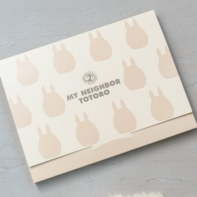 May include: A light beige box featuring a pattern of light brown Totoro silhouettes. The text "MY NEIGHBOR TOTORO" is printed in gray. The box has a light brown base.