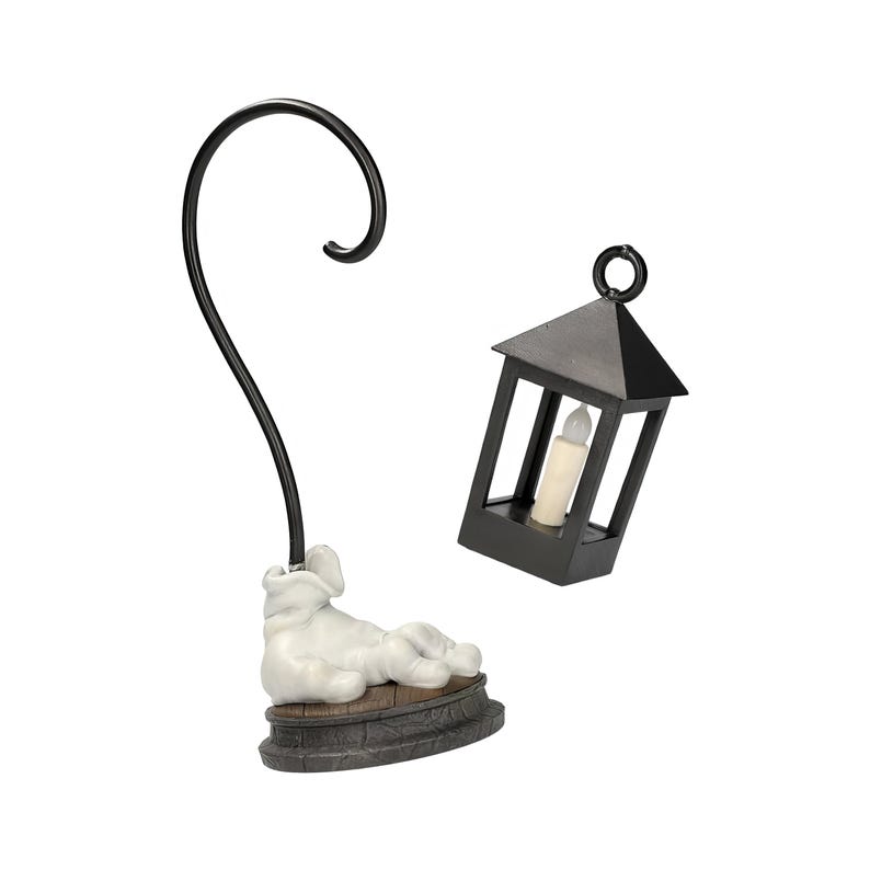 May include: A black metal lantern with a battery-operated candle and a matching black metal hook stand with a white figurine base. The lantern is a small, decorative item, perfect for adding a touch of ambiance.