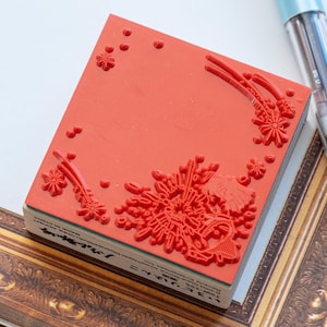 May include: A square rubber stamp with a red surface featuring an embossed design of a character, floral elements, and scattered dots. The side of the wooden block base displays black printed text including the words Studio Ghibli and Made in China.