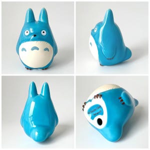 May include: A blue ceramic figurine of Totoro, a character from the animated film My Neighbor Totoro. The figurine has a white belly, large eyes, and pointed ears. The bottom of the figurine has the text "Studio Ghibli Sousei".