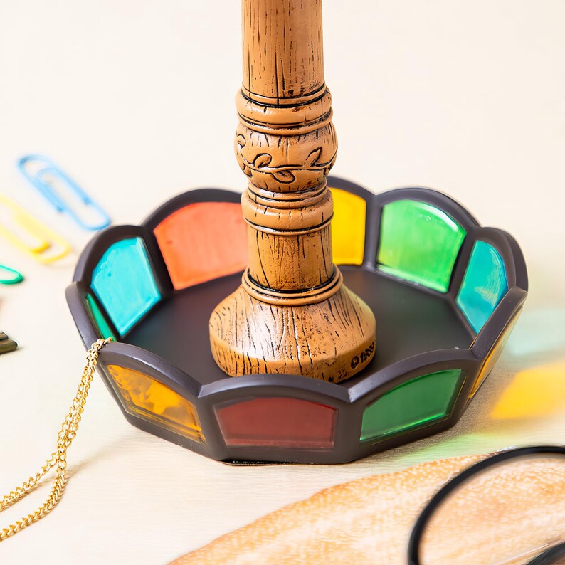 May include: A decorative, brown wooden lamp base with a stained glass tray. The tray features a black border and colorful glass panels in shades of blue, orange, yellow, red, and green. A gold chain is draped over the tray.