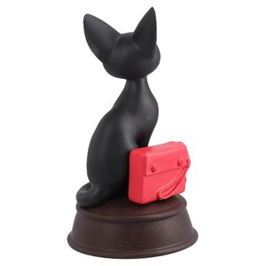 May include: A black cat figurine with a red purse, sitting on a brown base. The cat is stylized with pointed ears and a curved tail. The purse has a flap and a handle. The figurine is a decorative item.