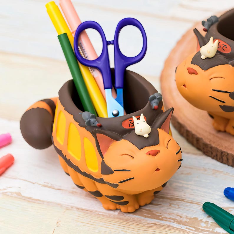 May include: An orange and brown cat-shaped desk organizer with yellow accents, holding pens and scissors. The organizer has a smiling face and small white and gray figurines. A fun and functional desk accessory.
