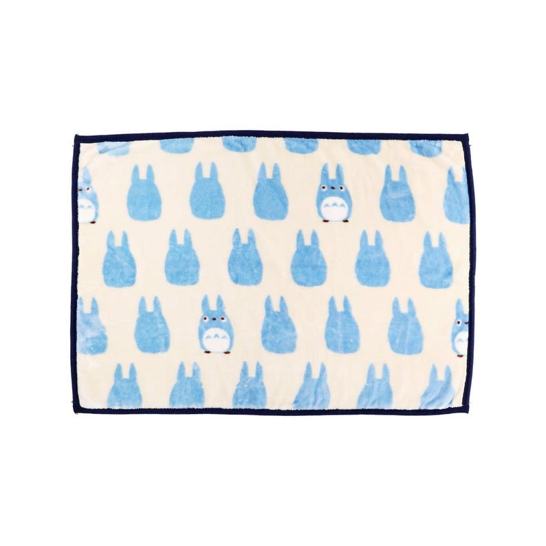May include: A rectangular, cream-colored blanket featuring a repeating pattern of light blue cartoon characters. The blanket has a dark blue border. The cartoon characters have white bellies and are in various poses.