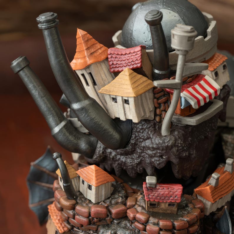 May include: A detailed sculpture of a fantasy creature with a fortress built on its back. The sculpture features miniature houses with orange and red roofs, a gray helmet, and black smokestacks. The creature's body is textured and dark brown.