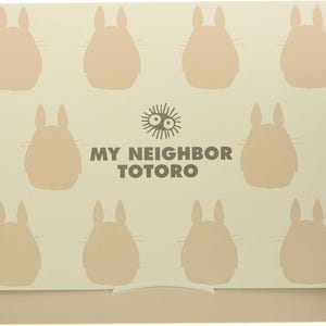 May include: A beige box featuring a pattern of light brown Totoro silhouettes. The words "MY NEIGHBOR TOTORO" are printed in dark brown, along with a sun-like graphic. The box has a simple, folded design.