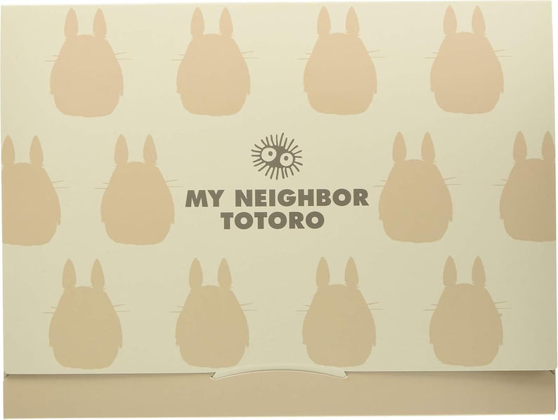 May include: A beige box featuring a pattern of light brown Totoro silhouettes. The words "MY NEIGHBOR TOTORO" are printed in dark brown, along with a sun-like graphic. The box has a simple, folded design.