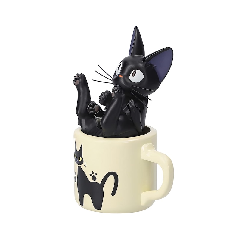 May include: A black cat figurine reclines inside a cream-colored mug. The cat has white eyes, whiskers, and pointed ears. The mug features a black cat silhouette and paw prints. The handle is curved.
