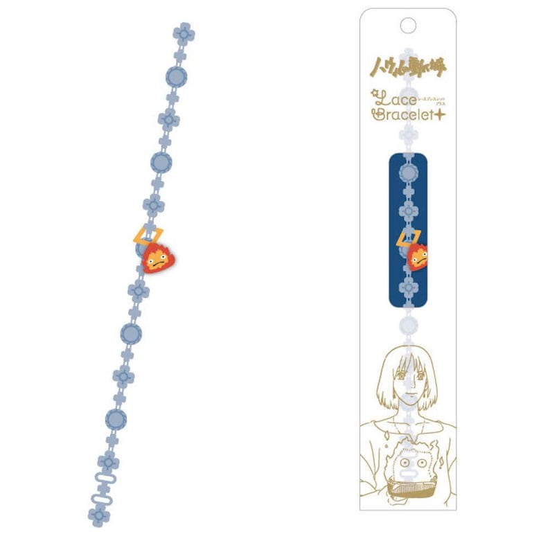 Op de afbeelding: Een lichtblauwe kanten armband met een cartoon vuur karakter bedel. De armband heeft bloem- en cirkelaccenten. De verpakking bevat de tekst "Lace Bracelet+" en een karakterillustratie.