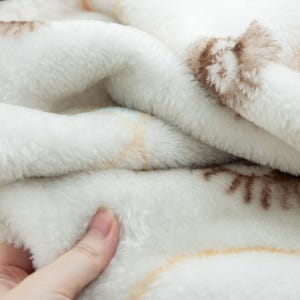 Peut inclure: Gros plan sur une couverture blanche et douce avec une texture en peluche. La couverture pr&eacute;sente un motif subtil dans les tons marron et beige. Le tissu semble chaud et invitant.