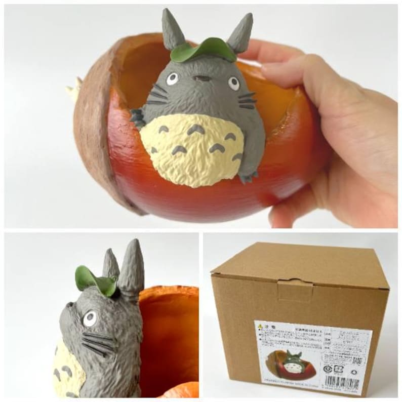 K&ouml;nnte beinhalten: Eine graue Totoro-Figur mit gr&uuml;nem Hut sitzt in einem rot-orangen Pflanzgef&auml;&szlig;. Der Pflanztopf hat eine braune Au&szlig;enseite und eine leuchtend orangefarbene Innenseite. Die Figur hat einen cremefarbenen Bauch mit gelben blattf&ouml;rmigen Markierungen. Das Bild zeigt auch einen Karton.