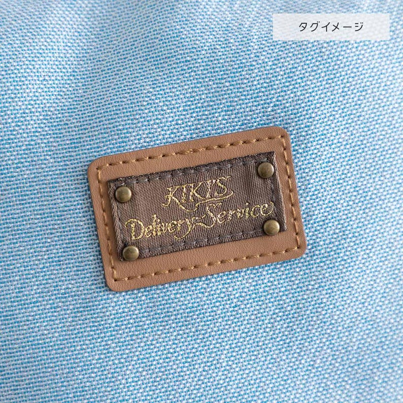 May include: A brown leather patch with the text "Kiki's Delivery Service" in gold lettering on a light blue fabric background.