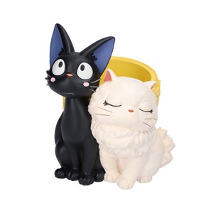 Puede incluir: Una maceta decorativa que presenta un gato negro de ojos grandes con orejas bordeadas en azul junto a un gato blanco esponjoso de ojos cerrados. El recipiente tiene un interior amarillo brillante y un exterior texturizado de resina lisa.