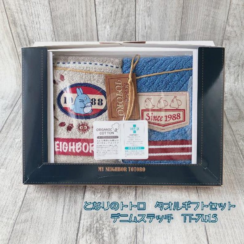 Puede incluir: Un juego de regalo en caja con dos toallas con el tema Mi Vecino Totoro. Una toalla es beige con un gr&aacute;fico de Totoro y el texto "EIGHBOR". La otra es azul con un parche "Since 1988". Incluye una etiqueta que dice "TOTORO".