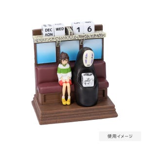 May include: A decorative figurine featuring characters from a Japanese animated film. The figurine includes a seated girl in a green and white striped shirt and a black figure with a white mask. A calendar displays the date.