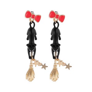 May include: A pair of dangle earrings featuring a red bow, a black cat, a gold-colored broom, and gold stars. The earrings are designed with a whimsical, Halloween theme.