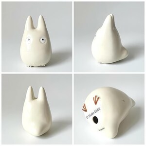 May include: A set of four images showcasing a cream-colored ceramic figurine. The figurine has a rounded body, two tall ears, and small, detailed facial features. The bottom of the figurine has the text "Studio Ghibli".