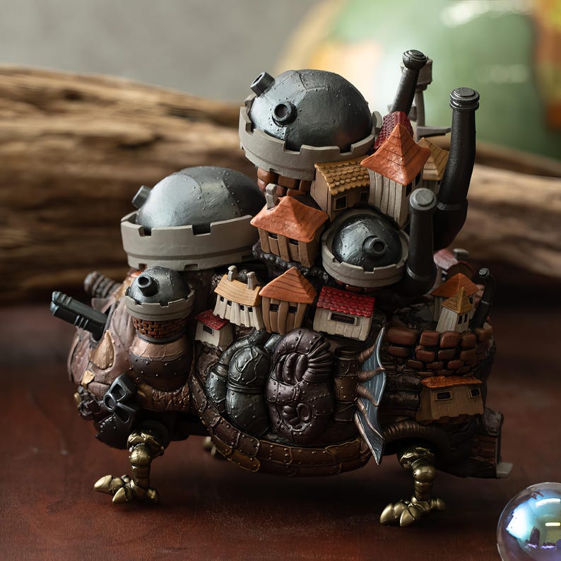 May include: A detailed, multi-layered sculpture of a moving castle. The castle features miniature houses with orange and brown roofs, set against a backdrop of metallic gray domes and chimneys. The base has a textured, brown and bronze finish, with golden claw-like feet.