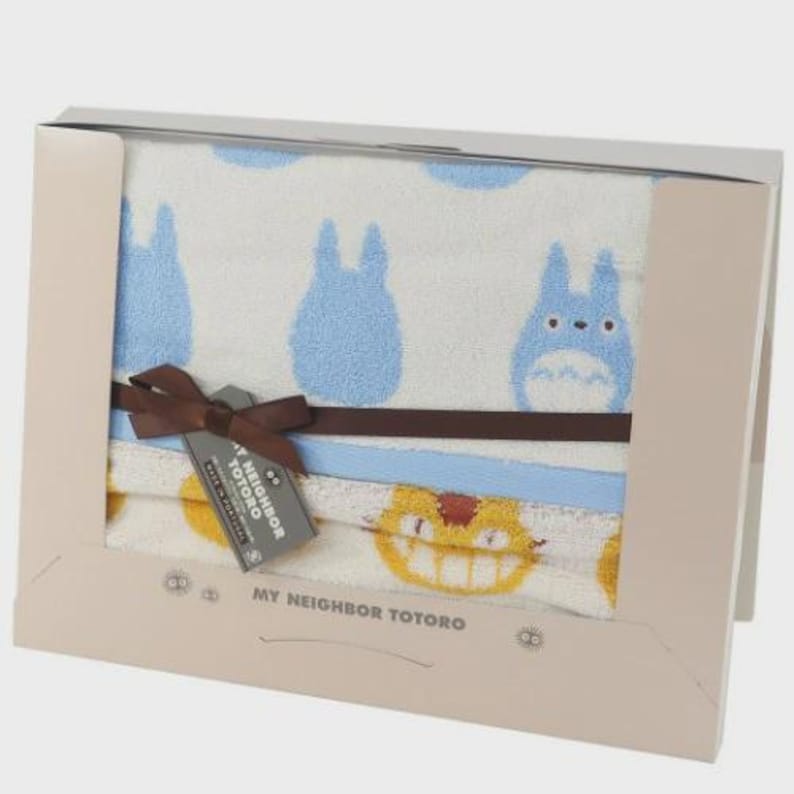 May include: A boxed set of towels featuring characters from "My Neighbor Totoro." The towels have a white background with blue Totoro figures and a yellow cat-bus design. A brown ribbon and tag are attached to the towels.
