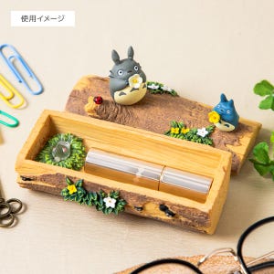 May include: A wooden pencil case with a decorative log design, featuring miniature Totoro figures, flowers, and a ladybug. The case holds a silver tube. The top of the case has a log design with two Totoro figures.