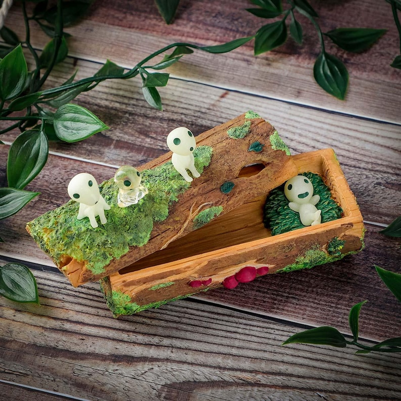 Pode incluir: Uma caixa de madeira em forma de tronco, adornada com figuras Kodama em miniatura. A caixa tem uma tampa articulada e um pequeno compartimento interior. As figuras Kodama s&atilde;o brancas com olhos pretos. A caixa &eacute; pintada com musgo.