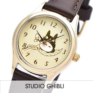 May include: A gold-tone watch with a brown leather strap features a Totoro character from the Studio Ghibli film My Neighbor Totoro. The watch face has a cream background with black Roman numeral hour markers and black hands.