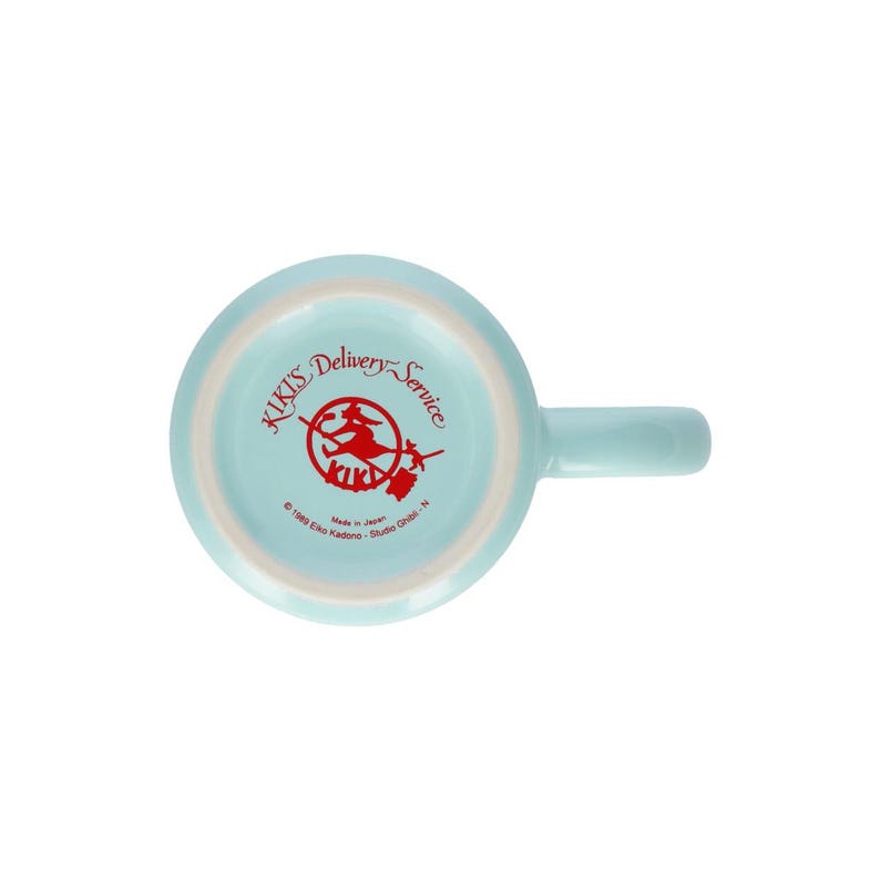 May include: A light blue ceramic mug viewed from the bottom, featuring a red graphic of a character on a broomstick. The text reads Kiki's Delivery Service, 1989 Eiko Kadono - Studio Ghibli - N, and Made in Japan, printed in red on the base.