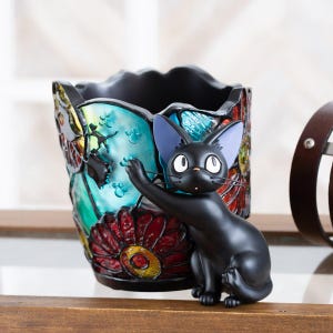 K&ouml;nnte beinhalten: Eine schwarze Katzenfigur mit blauen Augen, die auf einem bunten Bleistiftst&auml;nder aus Glas sitzt. Der St&auml;nder hat ein florales Design mit roten, gelben, blauen und gr&uuml;nen Akzenten.