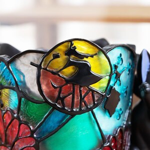K&ouml;nnte beinhalten: Ein Lampenschirm aus Buntglas mit einem bunten Schmetterlingsmotiv. Der Schmetterling hat gelbe, rote, blaue und gr&uuml;ne Fl&uuml;gel. Der Lampenschirm ist aus Glas und hat einen schwarzen Metallrahmen.