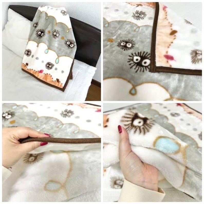 Peut inclure: Une couverture en peluche douce avec un motif r&eacute;p&eacute;t&eacute; de sprites de suie de dessin anim&eacute; sur un motif de nuages gris et blancs. La couverture a une bordure marron et est pli&eacute;e sur un lit.