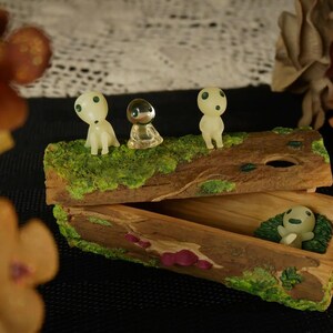 Pode incluir: Uma caixa de bugigangas de madeira com tampa articulada, decorada com musgo e figuras em miniatura. A caixa est&aacute; aberta, revelando uma figura dentro. Tr&ecirc;s figuras est&atilde;o em cima. Est&eacute;tica natural e terrosa.
