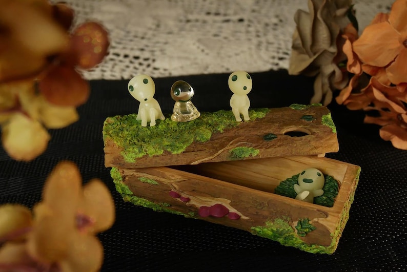 Pode incluir: Uma caixa de bugigangas de madeira com tampa articulada, decorada com musgo e figuras em miniatura. A caixa est&aacute; aberta, revelando uma figura dentro. Tr&ecirc;s figuras est&atilde;o em cima. Est&eacute;tica natural e terrosa.