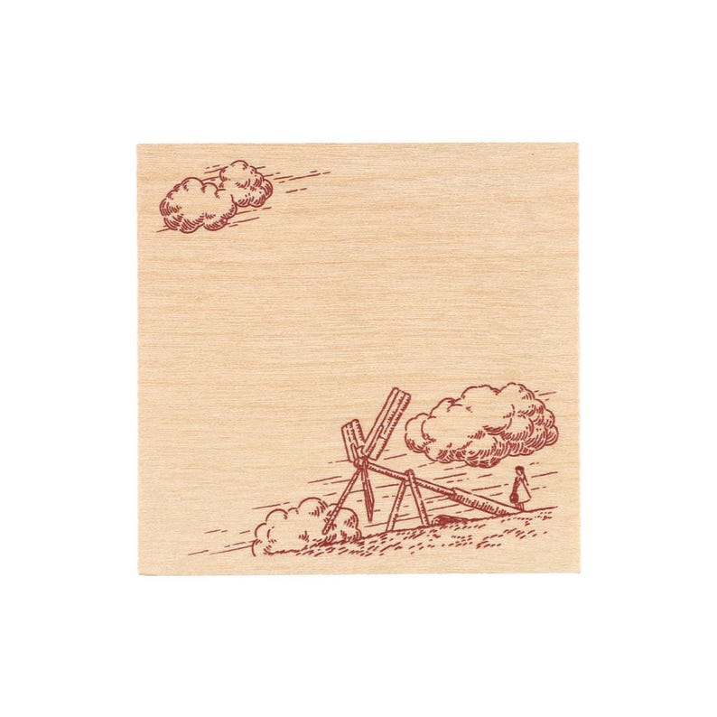 May include: A square wooden stamp featuring a dark red line art illustration of a windmill in a field with clouds in the sky and a small figure standing near the structure. The wood grain is visible across the surface of the stamp block.