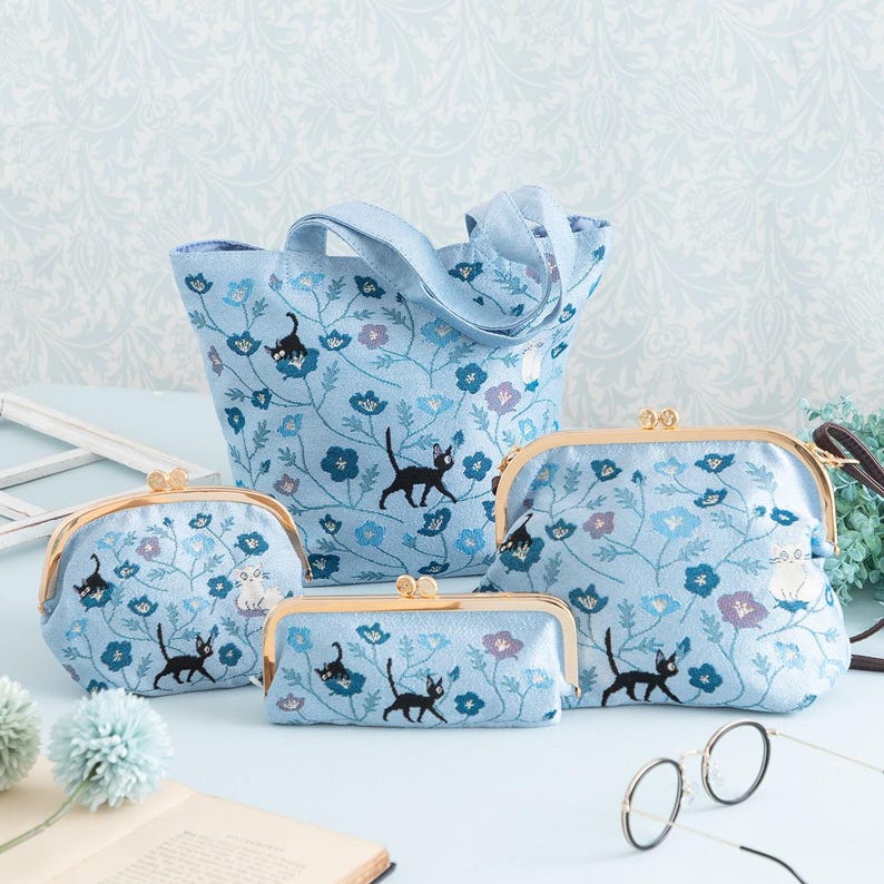May include: A set of four blue floral patterned purses with black cat embroidery. The set includes a tote bag, a large wallet, and two smaller wallets.