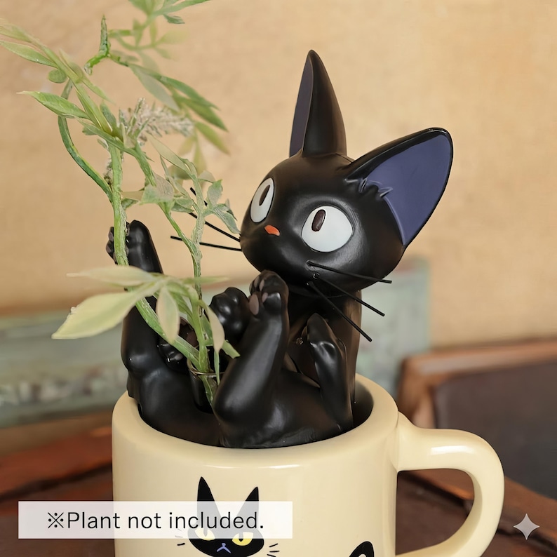 May include: A black cat figurine with large white eyes and a small orange nose, holding a green plant in a cream-colored mug. The mug has a black cat graphic. The text "Plant not included" is at the bottom of the image.