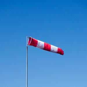 May include: A red and white windsock blowing in the wind against a clear blue sky.