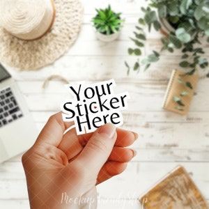 May include: A hand holding a white sticker with the text "Your Sticker Here" in black lettering.