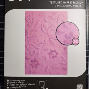 May include: A Sizzix Textured Impressions 3-D embossing folder by Catherine Pooler Designs. The packaging features a pink rectangular embossing folder with a floral pattern of flowers and leaves. A circular inset shows a close-up of the 3-D texture.