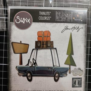 May include: A Sizzix Thinlits Colorize die set by Tim Holtz, model 666288, featuring 25 metal cutting dies. The packaging displays a blue car with luggage on the roof, a wooden sign, a green pine tree, and a cloud, all in a clear plastic bag.