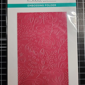 May include: A Spellbinders Paper Arts embossing folder, model SES-063, featuring a bold floral pattern. The packaging displays the text 'EMBOSSING FOLDER', 'Bold Floral', and '1 Folder 5.5 x 8.5 in'. The design shows embossed pink flowers and leaves.