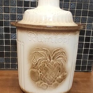 May include: White ceramic crock with a brown lid and a brown design of fruit and a pineapple. The crock has the word "Rumtopf" written on the front.