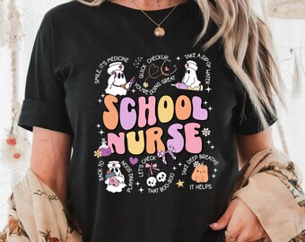 May include: Black t-shirt with a colorful graphic that reads "SCHOOL NURSE." The design includes cartoon ghosts, medical symbols, and phrases like "Smile, it's medicine" and "Take a sip of water."
