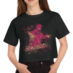 May include: A black cropped t-shirt with a pink and gold abstract design of a person dancing. The design is made up of small dots and splatters.