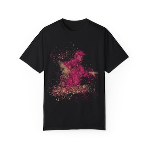 May include: Black t-shirt with a pink and gold splatter design of a person dancing.
