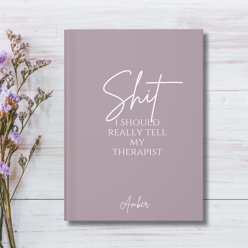 May include: A dusty mauve hardcover journal featuring the white text "Shit I SHOULD REALLY TELL MY THERAPIST" in a mix of script and serif fonts, with the name "Amber" printed in a script font near the bottom center of the front cover.